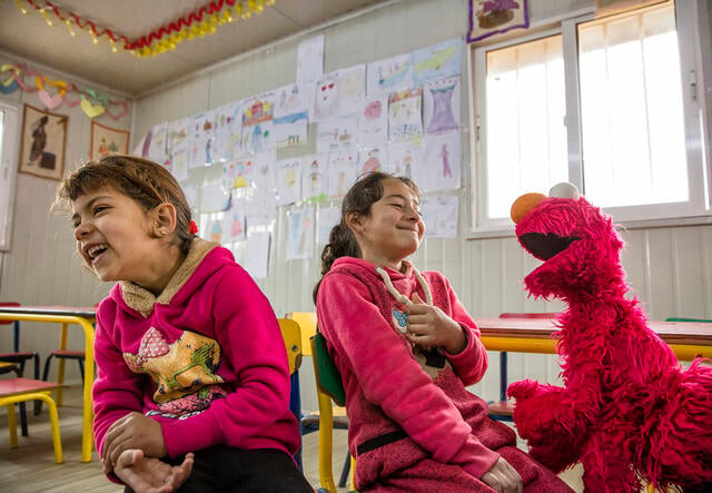 Two girls laugh with Elmo at a Ahlan Simsim location.
