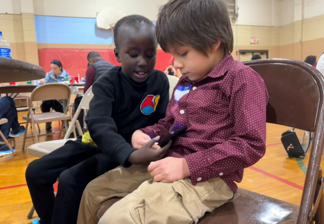 Two children sitting and looking at a phone.