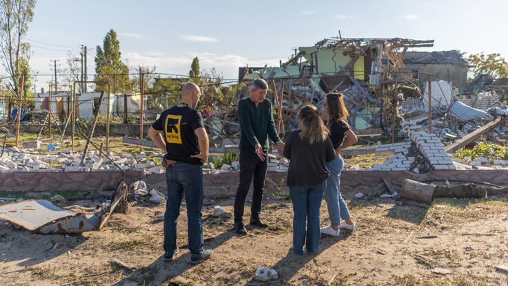 IRC team members meet with a local man in front of a building destroyed by a missile strike.