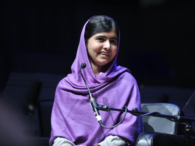 Malala yousafzai wearing purple headscarf speaking into microphone