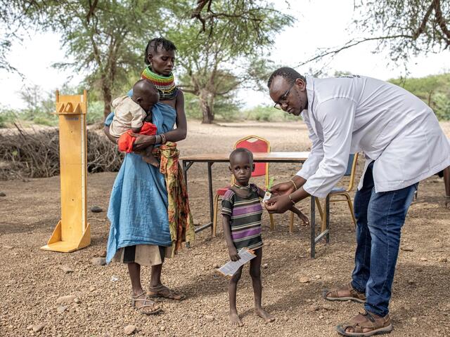 Two-year-old Kaliba is screened for signs of malnutrition by a malnutrition worker in Kenya. Kaliba's mother stands close by and watches the procedure.  