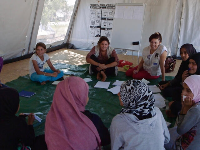 Girls sit in a circle playing a game in a tent that serves as an IRC "safe space" in a refugee camp in Greece. 