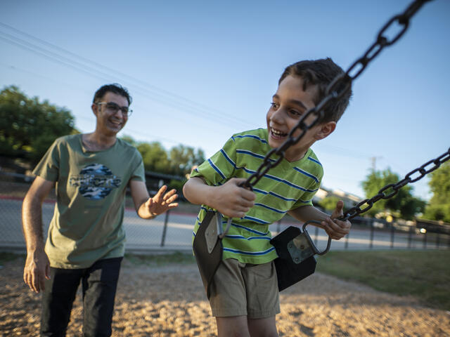 Iraqi refugee Junaid pushes his son on a swing in a park in Dallas, Texas