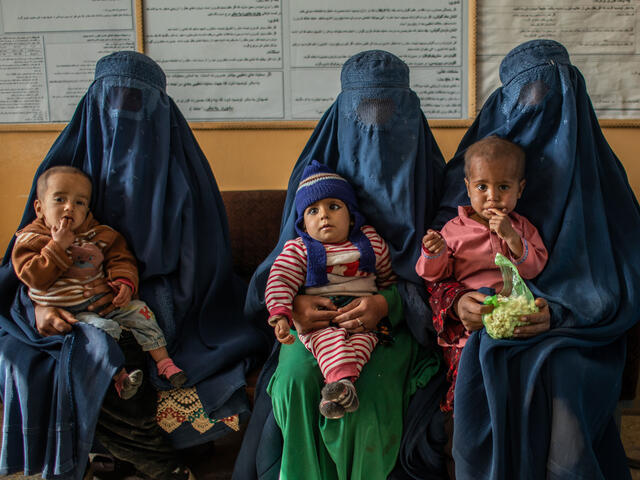 Three woman sit in a line at an IRC-supported clinic in Afghanistan. All have children on their laps. 