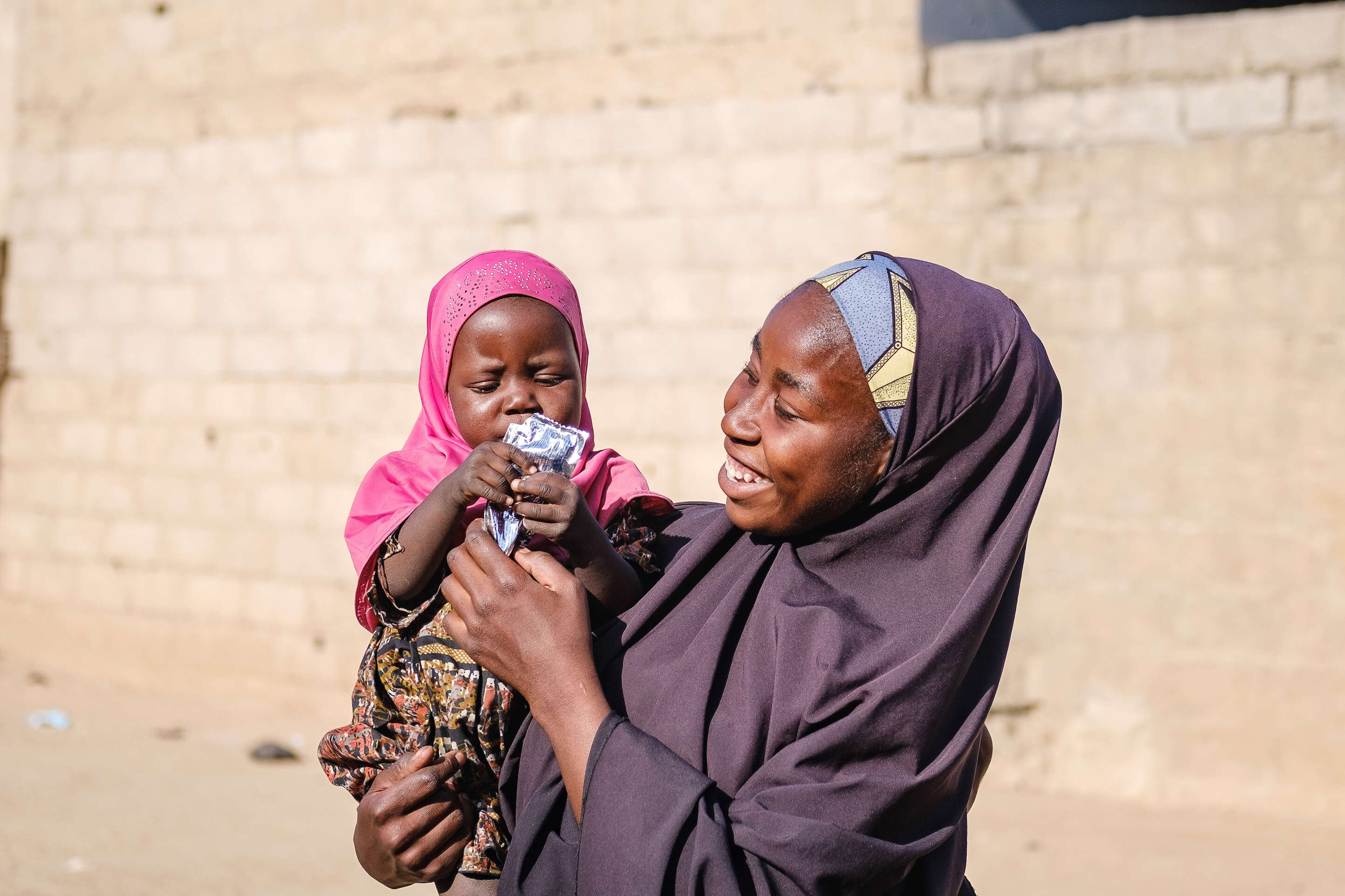 나이지리아의 한 엄마가 자녀에게 영양실조치료식을 먹이면서 웃고 있습니다. 