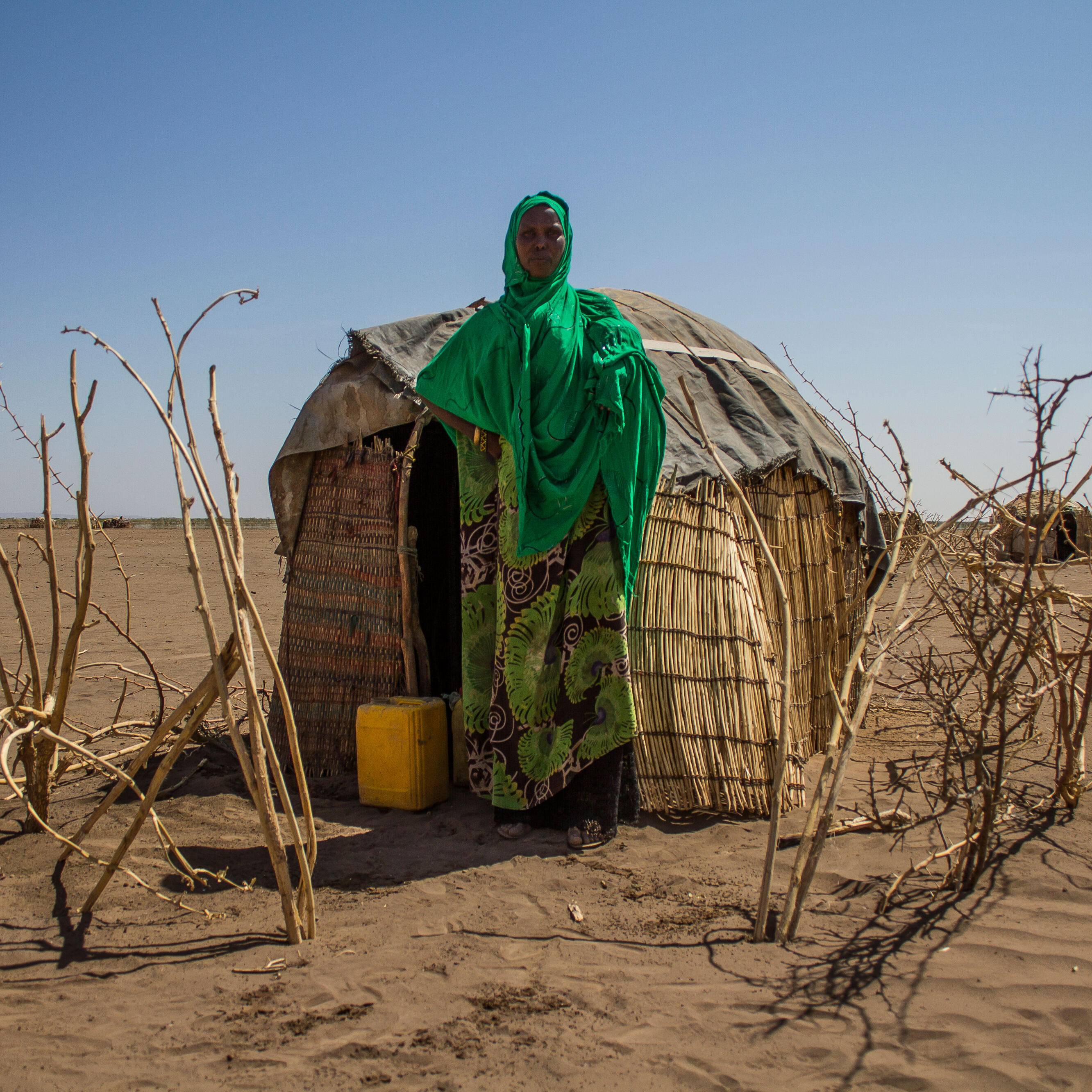 Woman stands in front of temporary shelter in drought-afflicted region.