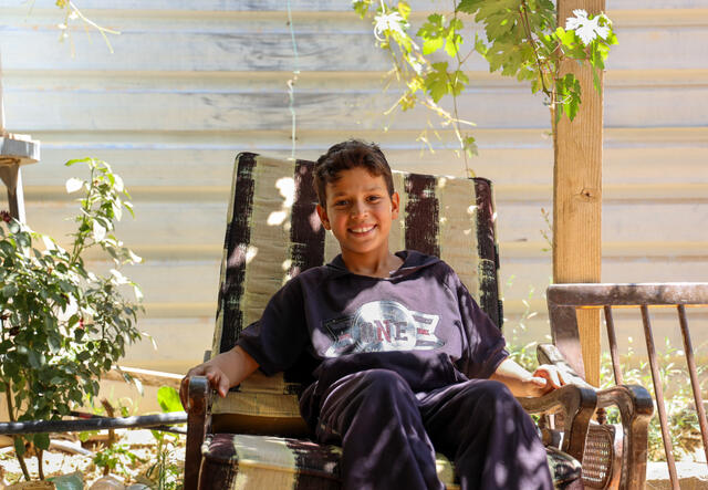 A 10-year-old Syrian boy sits in a chair outside under the shade of a grapevine arbor in a refugee camp in Jordan