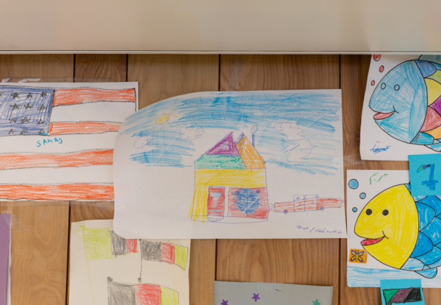 Children's drawings hang on the walls of a U.S. processing center. The pictures include a house, a fish and an American flag.