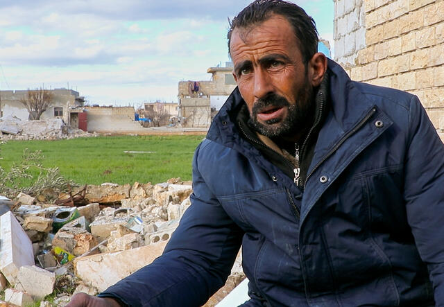 A Syrian man, Faisal (not his real name), stands outside in the cold with rubble behind him after the Feb. 6, 2023 earthquake.