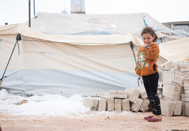Farah stands outside her family's tent. Snow covers the ground around her.