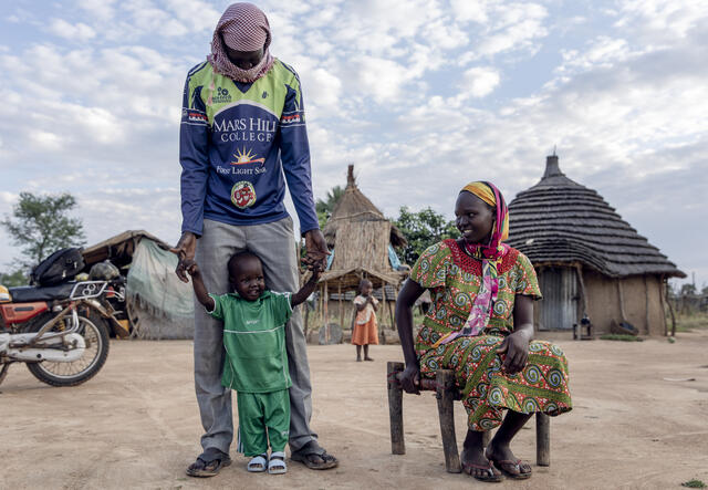Peter steht neben seiner Mutter und seinem Vater vor ihrem Haus im Südsudan.