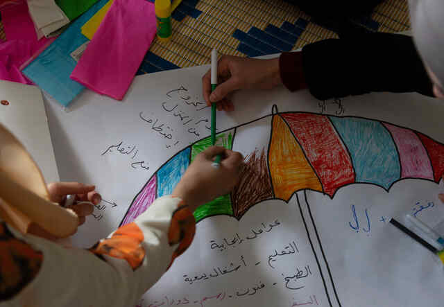 Syrian refugee girls color and write on a piece of paper on the floor in the safe space where they take part in different kind of activities with the IRC WPE team.