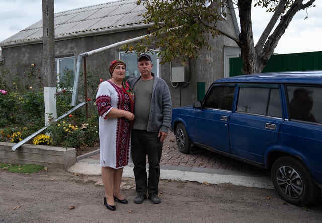 올가는 우크라이나에 있는 그들의 집 앞에서 그녀의 남편 옆에서 사진을 찍기 위해 포즈를 취하고 있습니다. 비록 그들의 집은 파괴되지 않았지만, 전쟁은 이 지역에 심각한 영향을 미쳤고 두 사람은 오랜 시간 동안 지하로 피신해야 했습니다.