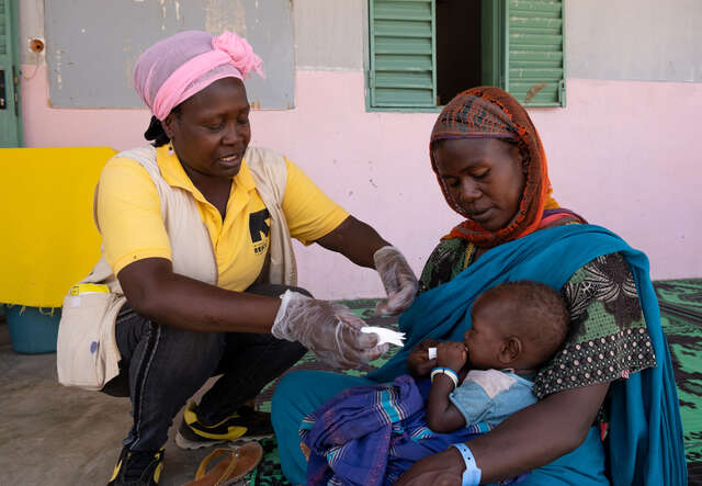 IRC-Gesundheitshelferin Martine Naigna gibt der neun Monate alten Salima ein Päckchen mit Erdnusspaste.
