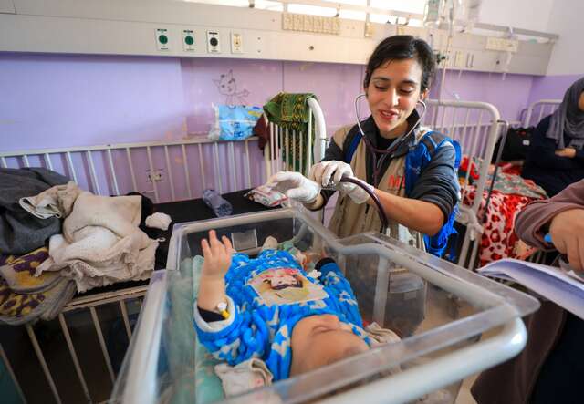 Dr. Jilani beugt sich vor und lächelt ein Baby an, das sie im Al-Aqsa-Krankenhaus in Gaza behandelt.