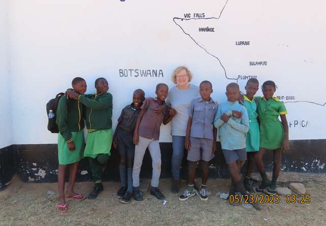 Housing Volunteer, Sylvia, visits school in Zimbabwe and takes a photo with the students.