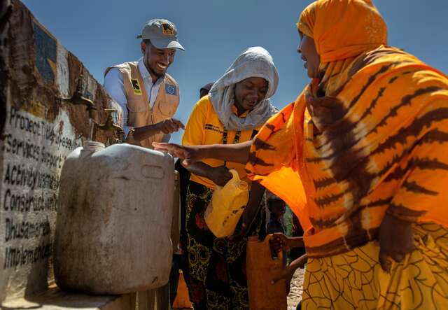 IRC staff members assist women collecting water from safe water collection points.