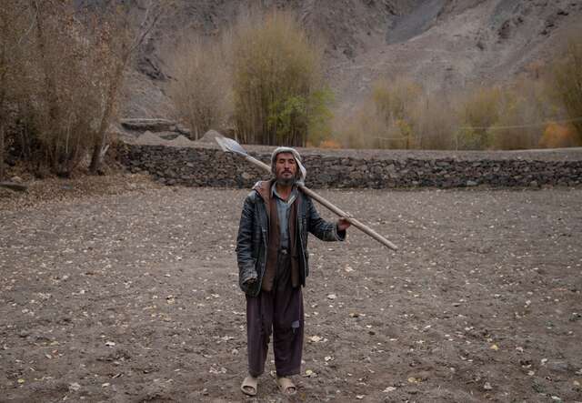 A farmer holds a shovel over his shoulder and stands in the middle of his potato farm in Afghanistan.