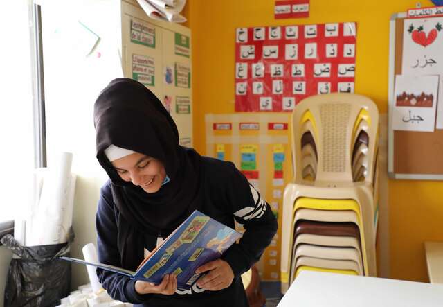Girl in a classroom smiles whilst reading a book.