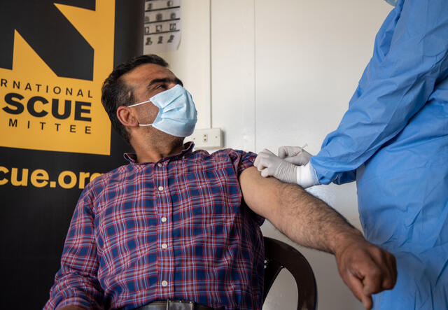 A Syrian man sitting with his sleeve rolled up receives a COVID-19 vaccination from a nurse at an IRC clinic in Zaatari refugee camp in Jordan