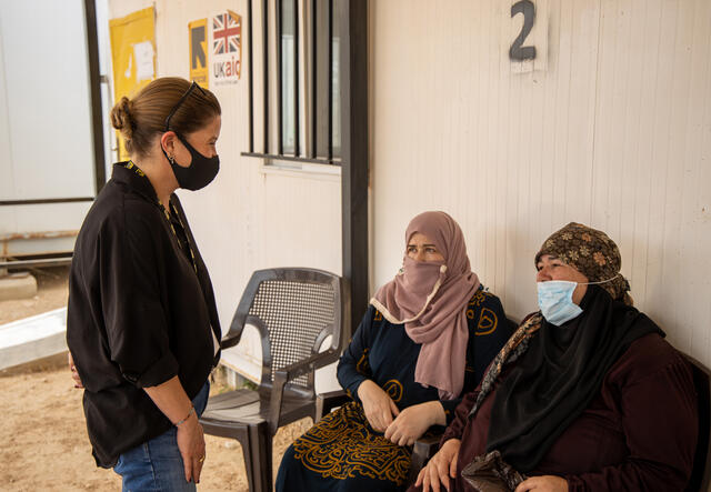 Sarra Ghazzi, IRC country director in Jordan stands speaking with two seated Syrian women waiting to get COVID-19 vaccinations at an IRC clinic.
