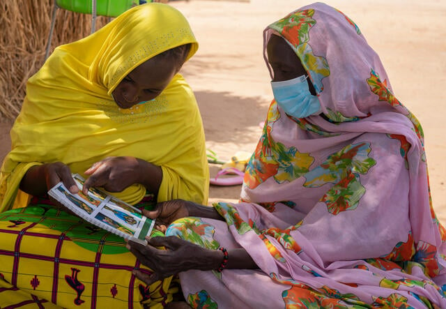 Two women in Niger sit on a mat reviewing a health training manual together.