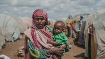 Mother stands holding her 12 month baby, in Daryel Shabellow IDP camp, Somalia.