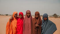 Five girls dressed in bright colours smile at the camera.