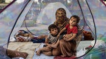 A woman holds her two children as they sit inside a tent