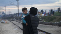 A woman walking down train tracks with her child.