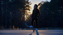 Against a forest sunset, Belqisa stands on her skateboard 