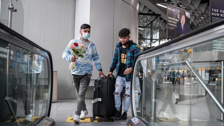 Afghan refugee Mehdi, 29, carrying a bouquet of flowers, helps his 17-year-old brother Ali with his luggage after Ali's flight to Frankfurt airport.