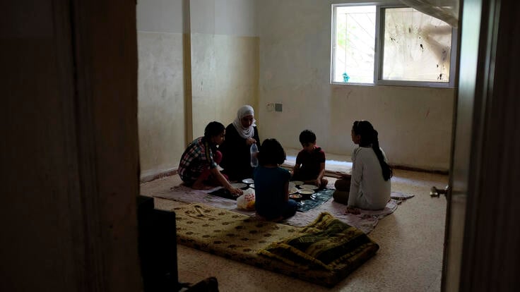 Amira and her four children sit together on the beige tiled floor in their apartment for a late lunch.