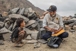 An IRC employee sitting with a young boy in front of rubble