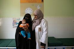 A female doctor stands beside a woman and her baby