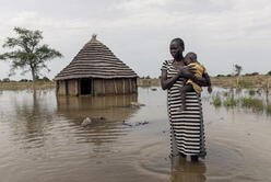 Eine Frau hält ihr Kind im Arm und steht auf einer überfluteten Wiese.