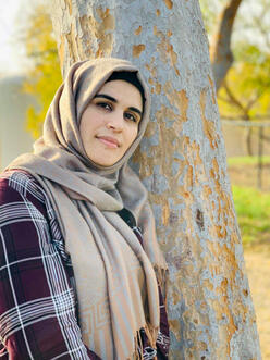 Khalida stands leaning against a tree