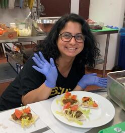 A woman with glasses smiling with her hands presenting a plate of falafel.