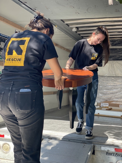 Two IRC staff members carry a coffee tables out of a u-haul