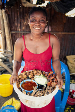Wara stands smiling holding food from her business.