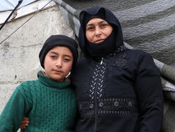 Mother and child standing shoulder to shoulder outdoors in Syria. They are wearing warm clothes.