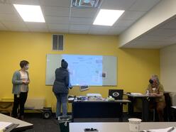 Two IRC staff members observe while a New Roots gardener participates in an activity on the whiteboard. 