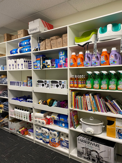 A view of the Resettlement store which contains toilet paper, cleaning supplies, laundry detergent, toothpaste, children's books. All of these items are displayed on shelves