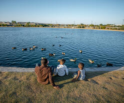 Three kids looking out to a pond.