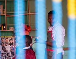 Nelson cutting the hair of a client at his barbershop in Kampala, Uganda