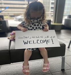 Child holding a sign that says "WELCOME!" in both English and Pashto
