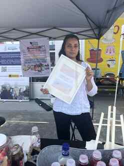 Hetal Soni at the Yogi Elixir tent at the Small Business Pop Up at Refuge Coffee, holding up a sign for her business.