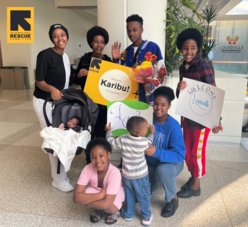 A family of eight smile together and hold welcome signs at the Louisville airport. 