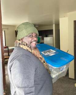 A man smiling carries a large container during a housing move-in.