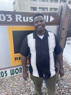 A man smiling stands outdoors, in front of the IRC in Missoula street sign.